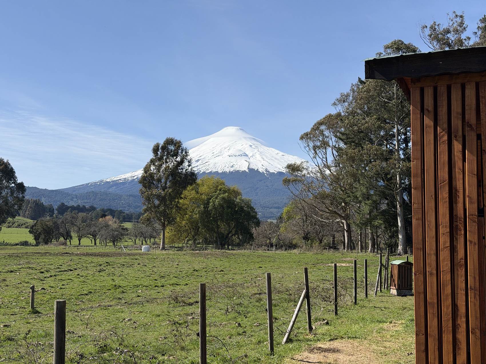 Campo verde con cercos de madera y el volcán Osorno al fondo
